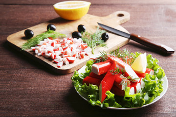 Crab sticks with lettuce in plate on a brown wooden table