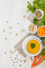Pumpkin cream soup with croutons, raw fresh pumpkin pieces  and herbs on a white rustic wooden background