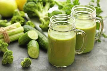 Bottles of juice with broccoli, celery and cucumber on grey wooden table