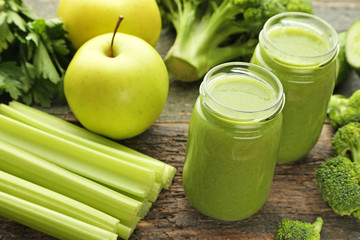 Bottles of juice with broccoli, celery and cucumber on grey wooden table