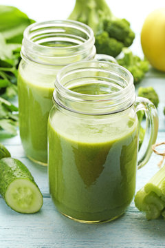 Bottles of juice with broccoli, celery and cucumber on white wooden table