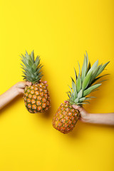 Female hands holding ripe pineapples on yellow background