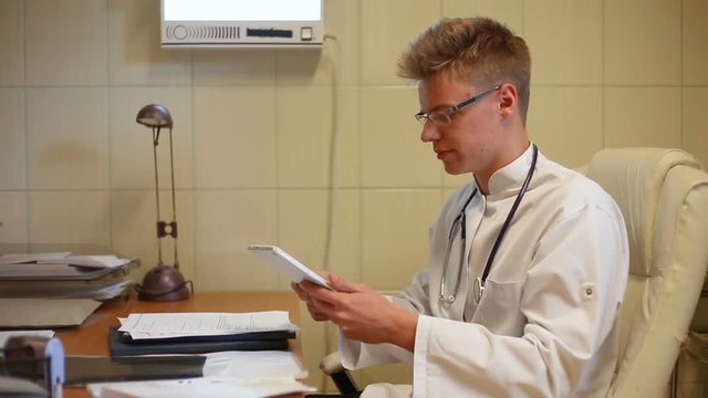 Doctor using tablet and doing serious look to the camera in the office
