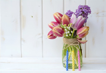 bouquet of tulips and lilac with birthday candles  on a white wooden background