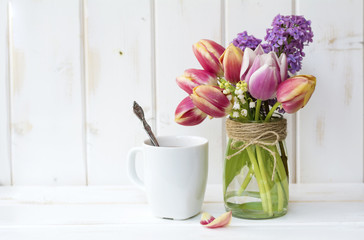 cup of coffee with milk and bouquet of lilac on white wooden background