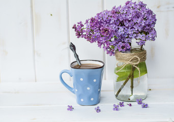 cup of coffee with milk and bouquet of lilac on blue wooden background