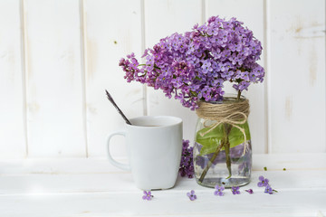 cup of coffee with milk and bouquet of lilac on blue wooden background
