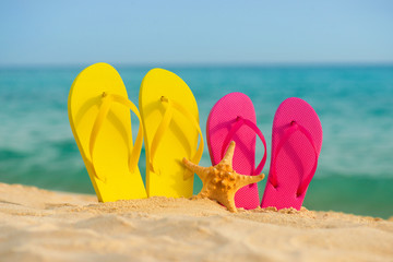 Sea-stars with yellow and pink sandals stand in the sand against the background of the sea.