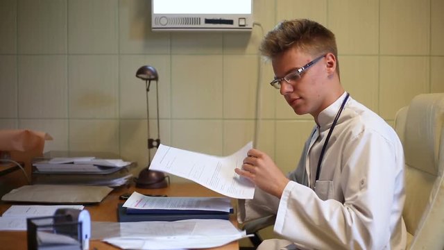 Doctor looks busy while sitting in the office and working on papers
