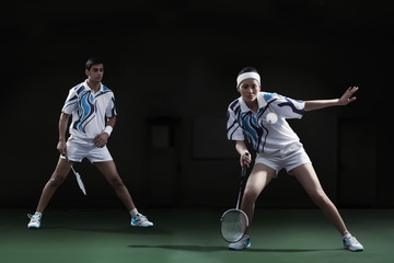 Woman hitting shuttlecock with badminton racket with partner looking at her