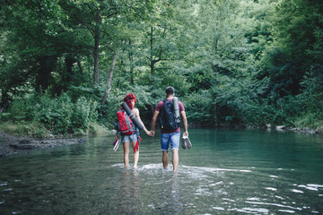 Happy young hikers couple enjoying in adventure. They camping and having fun while walking through the wild mountain river.