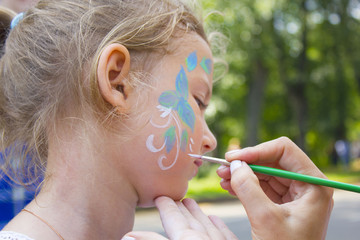 little girl getting her face painted like a butterfly by face painting artist.