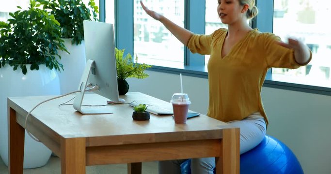 Female executive doing exercise on exercise ball at her desk