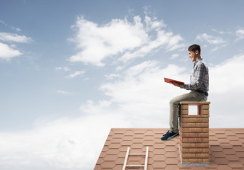 Handsome man on brick roof against cloud scape reading book