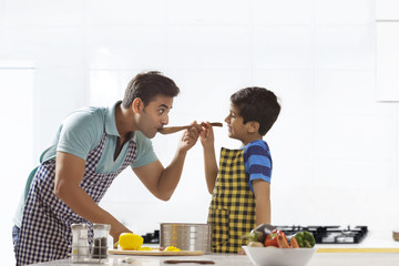 Father and son tasting soup while cooking in kitchen