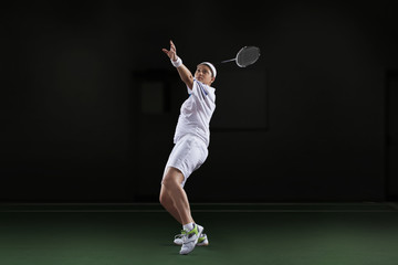 Side view of young woman in sportswear playing badminton isolated over black background
