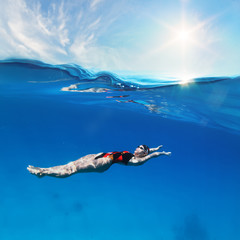 Female professional swimmer swimming on back under waterline with sunshine above