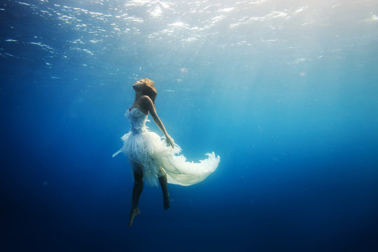 Drawning girl in white dress in deep blue ocean. Underwater shot
