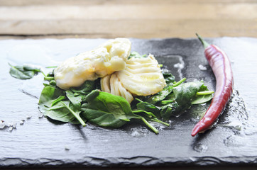 White fish fillet with chili on fried spinach. Gray background.