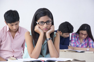 Portrait of bored female student with friends in background at classroom