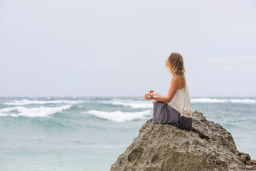 Girl sit at the seaside on the rock and meditating in yoga woman pose