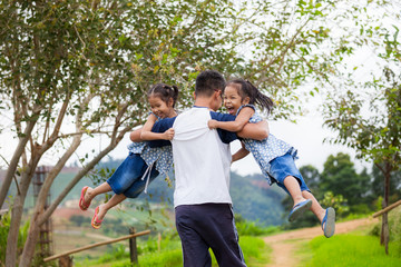 Asian father carrying two child girls and spinning around with fun in the park