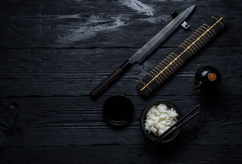 Japanese cuisine. Rice, soy sauce and chef knife over dark wooden background.