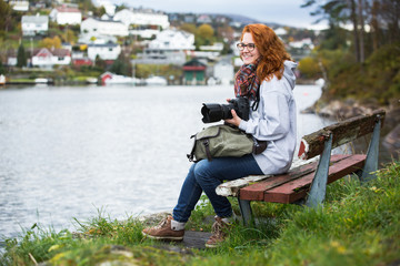 Girl photographer with red hair sitting on a wooden bench in Scandinavia