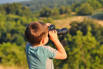 Boy looks through the binoculars. Little boy travel in nature and look into mountains 