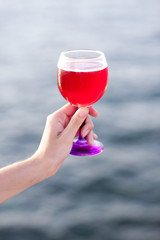 Girl holding glass of red lemonade over sea background.