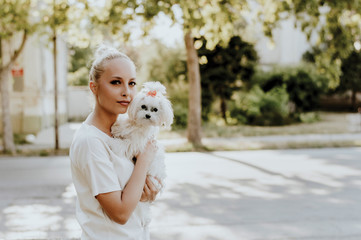 Smiling woman holding a maltese dog in park.
