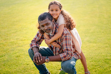little happy african american granddaughter hugging her grandfather on green lawn