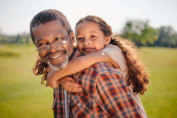 happy african american granddaughter hugging her smiling grandfather on green lawn
