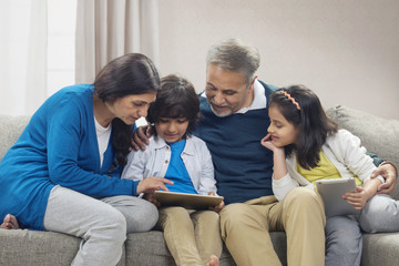 Grandchildren using digital tablet with grandparents sitting on sofa