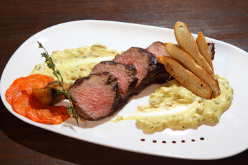 Appetizing steak medium roast, cut into pieces in creamy mushroom sauce. Steak served on white plate on a wooden table.