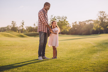 african american granddaughter and her grandfather holding hands and standing on green lawn
