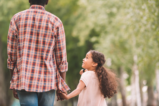 african american granddaughter holding hands with grandfather and walking in park