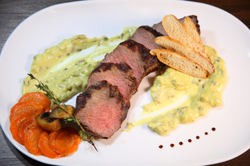 Appetizing steak medium roast, cut into pieces in creamy mushroom sauce. Steak in a white plate on a wooden table.