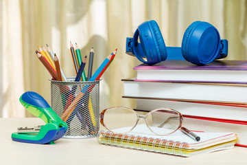 School supplies. Books, headphones, colour pencils, glasses, notebook, pen, stapler on wooden table