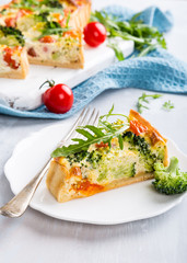 Slice of delicious vegetarian homemade quiche with cherry tomatoes and broccoli on white plate. Healthy food concept.