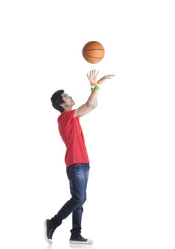 Side view of young boy in casuals tossing basketball over white background 