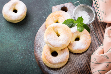 Homemade baked donuts with powdered sugar on green background. Selective focus. Copy space.