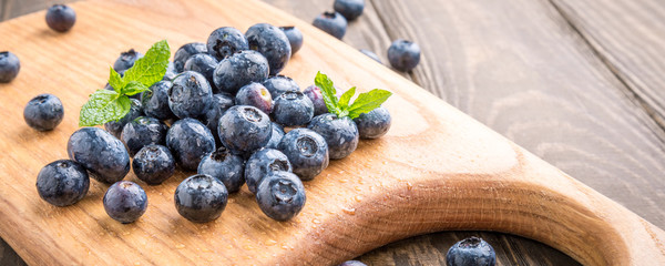 Fresh blueberries on cutting board on old wooden background. Healthy eating and nutrition concept. Banner.