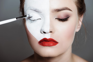 young beautiful teen girl applying creative white bodyart with makeup brush on face, isolated on grey