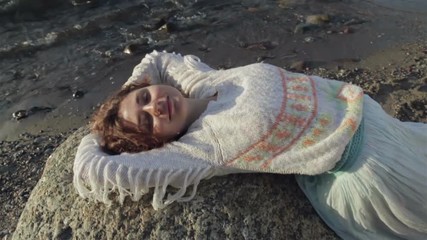 Red-haired girl is lying on a large rock on the beach.