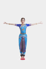 Portrait of young woman with arms outstretched performing Bharatanatyam against white background