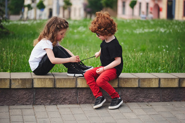 boy helps little girl tie shoelaces - obrazy, fototapety, plakaty