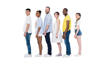 side view of young multiethnic people standing in row and smiling at camera isolated on white