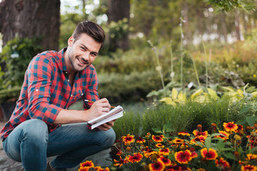 smiling gardener with notebook in hands looking at camera in garden