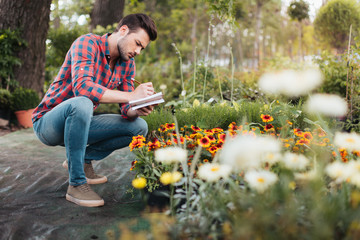 side view of focused gardener making notes in notebook while checking plants in garden